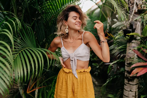 Mujer encantadora energética con peinado corto con pantalones cortos amarillos y baile superior y divertirse al aire libre en el día de verano —  Fotos de Stock