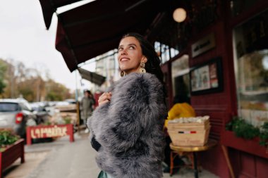 Uzun dalgalı saçlı, kürklü, romantik, modern bir kadın. Rüya gibi duygular ve gerçek bir gülümsemeyle gözlerini kaçırıyor.