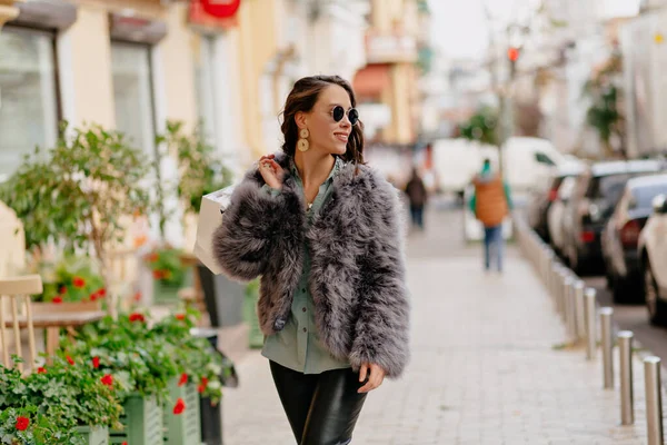 Stylish modern woman wearing fur coat and leather pants walking on bright street and has fun after shopping — 스톡 사진