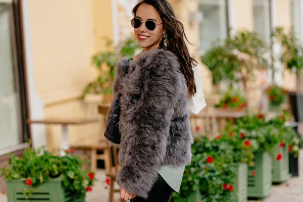 Pretty woman wearing glasses and fur coat walking on the street and smiling on good day — 스톡 사진
