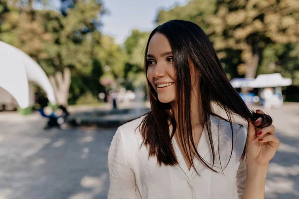 Mujer bonita romántica con el pelo oscuro jugando con su pelo y mirando a un lado con sonrisa tímida — Foto de Stock