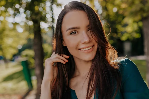 Ritratto ravvicinato di bella giovane donna con i capelli scuri sorridente alla macchina fotografica sul parco solare della città — Foto Stock