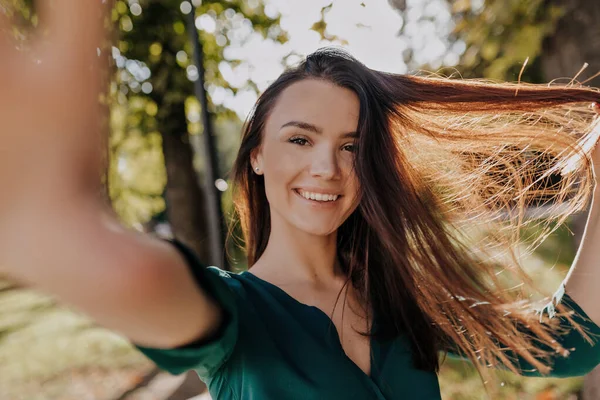 Feliz saída jovem senhora se divertindo fora no ensolarado parque da cidade, brincando com o cabelo e fazendo selfie — Fotografia de Stock