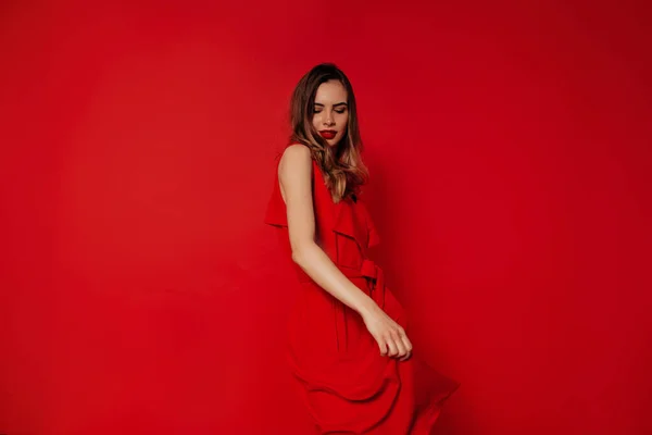 Игривая очаровательная леди в красном платье танцует и веселится в студии на красном фоне — стоковое фото