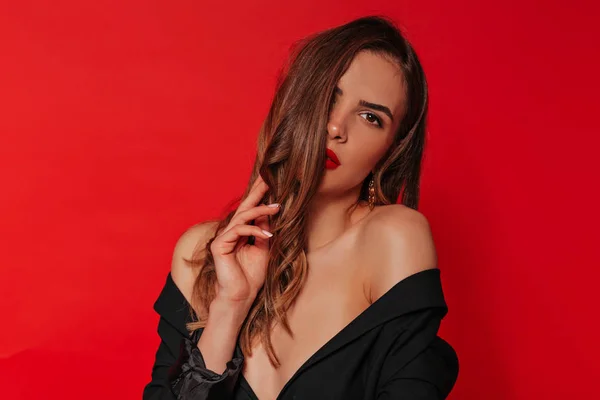 Primer plano retrato interior de una mujer con estilo fantástico posando con lápiz labial rojo usando chaqueta negra con hombros desnudos sobre fondo rojo —  Fotos de Stock