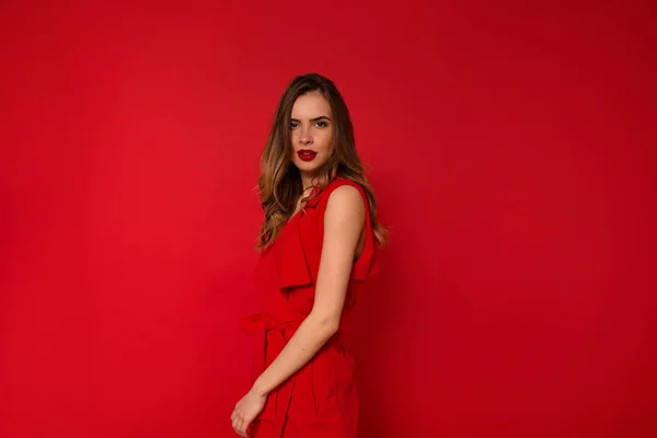 Женщина в праздничном красном платье с красными губами позирует перед камерой на изолированном красном фоне — стоковое фото