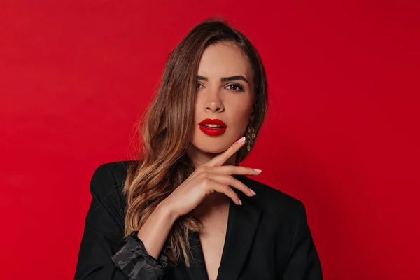 Mujer adorable con maquillaje de noche posando sobre fondo rojo tocando su cara y mirando a la cámara Imágenes de stock libres de derechos