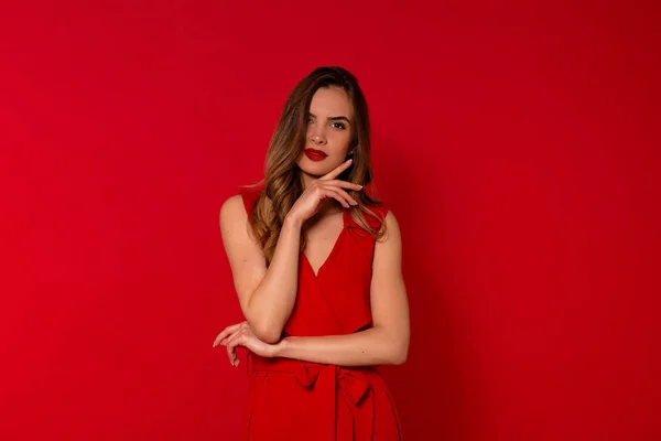 Retrato de chica encantadora sonriente en vestido rojo posando a la cámara. Foto interior de la espectacular dama de pie sobre fondo rojo —  Fotos de Stock