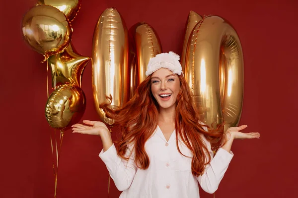 Close up inside portrait of happy smiling woman posing over red background with gold balloons in sleeping suit — Stock Photo, Image