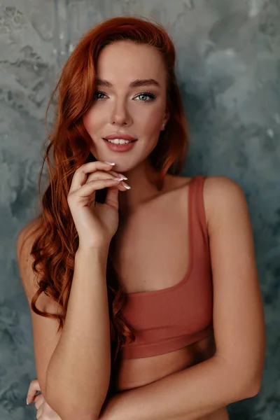 Ritratto interno di affascinante donna dai capelli rossi con i capelli ondulati e grandi occhi blu in posa davanti alla fotocamera sopra la parete grigia — Foto Stock