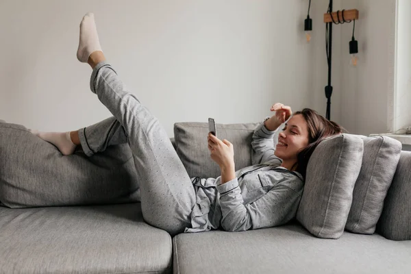 Full-lenght tiro indoor de mulher feliz em casa roupas rolando smartphone enquanto deitado no ônibus em dia ensolarado Fotos De Bancos De Imagens