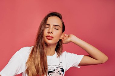 Beyaz tişört giyen neşeli, genç bir kadın, neşeli ve büyüleyici bir gülümsemeyle gözlerini kapatıyor. Öğrenci kız üniversiteden sonra evde dinleniyor.