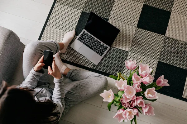 Frame above of working woman at home on quarantine with laptop and smartphone on background of stylish apartment with flowers . Work at home, isolation at home