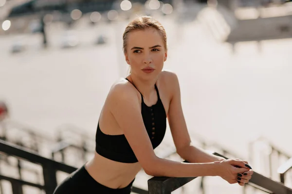 Retrato exterior de mujer joven atractiva con pelo recogido usando uniforme deportivo descansando durante el entrenamiento en verano día cálido —  Fotos de Stock