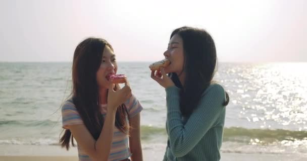 スローモーション 人生を楽しむ女性の友人は ビーチで甘いおいしいリラックスして自由をドーナツを食べます アジアの女性旅行者のライフスタイルの魅力的な一緒に Uhd映像 — ストック動画