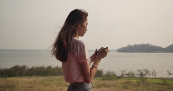 旅行者の若いアジアの女性は 日没の森林山の川の湖でフィルムカメラで写真を撮る 幸せな旅行の自然屋外 超スローモーションC4Kシネマティックカメラ映像 — ストック動画