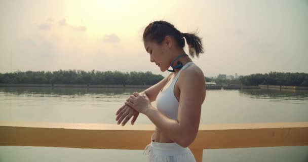 スローモーション 女性アスリートは 時計やリスニング音楽ガジェットを使用して実行する準備ができて ランナーは ジョギング運動プロの川側の朝の健康的な人々のライフスタイルに適合 — ストック動画