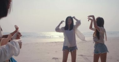 Gülümseyen Mutlu Arkadaşlar genç Asyalı kadın grubu dansları, plaj tatilinde ukulele şarkıları çalmaları, bagaj hatchback araba yolculukları ve seyahat hafta sonları, araba konseptiyle yolculuk etmeleri.