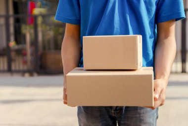 Maske takan Asyalı teslimatçı, kargo kartonunda bir paket gönderdi. Virüs tıbbi konsepti yayarken kargo sosyal mesafesini belirledi..