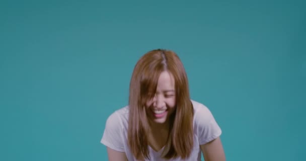 コピースペースで撮影された青の背景スタジオで白いTシャツに興奮して幸せな感情的な冗談顔を持って笑顔若いアジアの女性の笑顔 — ストック動画
