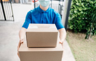 Maskeli teslimatçı, virüs yayılırken ve Coronavirus covid-19 ön ev müşterisini koronavirüs krizini önlerken ön alıcıya bir paket karton gönder..