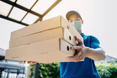 Maske takan Asyalı Teslimatçı, virüs yayılırken ve Coronavirus covid-19 ön ev müşterisini koronavirüs krizini önlerken eve pizza siparişi gönderiyor..