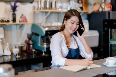 Asyalı kadın Barista müşteriyle ön tarafta iş, part-time iş ya da sahip olduğu iş kadını arıyor. Mutlu bir satıcı ve içecek hazırlıyor.