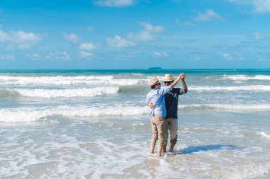 Asyalı yaşlı çift emekli oluyor. Dinleniyor. Gün batımında, sahil balayı ailesinde dans ediyor.