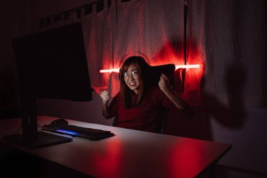 Profesyonel oyuncu oyunları kazanıyor. Genç Asyalı kadın çevrimiçi FPS turnuvası oynuyor. Gece kırmızı neon ışıklı oda, oyun kulaklığı ve klavye ile siber internet sıralanıyor..