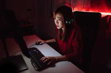 Profesyonel oyuncu genç Asyalı kadın çevrimiçi video oyunu oynuyor FPS turnuvası vuruyor gece kırmızı neon ışık odasında internet sıralaması yapıyor oyun kulaklığı ve klavye ile şampiyonluk etkinliğinde.