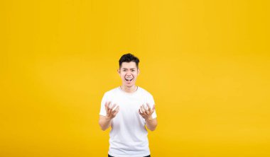 Saldırgan Asyalı genç adam öfke ve öfkeli negatif duygu sarı arka planda beyaz tişört giyip fotokopi çekilen, öfkeli ve mutsuz insanlar konsepti ile izole edilmiş stüdyo görüntüsü..