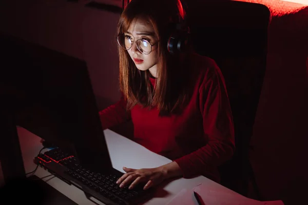 Pro player gamer young asian woman playing online video game shooting fps tournament ranking cyber internet at night red neon light room with gaming headset and keyboard on championship event.