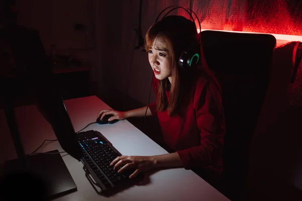 Pro player gamer young asian woman playing online video game shooting fps tournament ranking cyber internet at night red neon light room with gaming headset and keyboard on championship event.