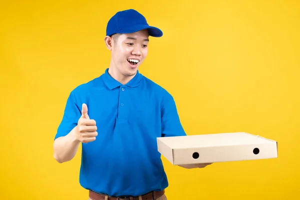 Delivery express of pizzaman asian male showing box delicious fast deliver to receiver shipping buying online order wearing blue uniform on yellow background isolated studio shot.
