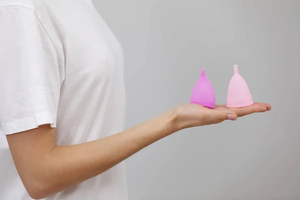 Rózsaszín menstruációs csésze. Közelkép a női kézről, ahogy különböző menstruációs poharakat tart. Női egészségügyi koncepció, nulla hulladék alternatívák — Stock Fotó