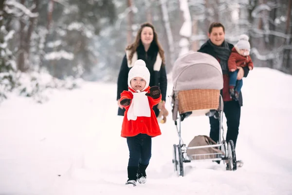 A beautiful family with retro pram walks through the winter snowy forest. Mother, father, daughter and baby son enjoying day outdoors. Holidays, christmas, happiness together, childhood in love.