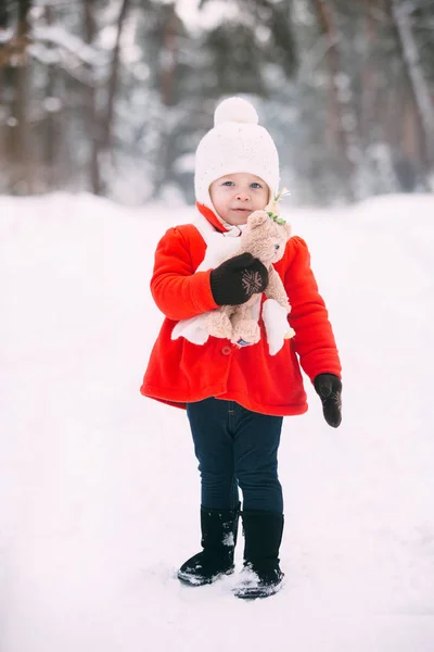 Little girl in red coat with a teddy bear having fun on winter day. girl playing in the snow — Stock Photo, Image