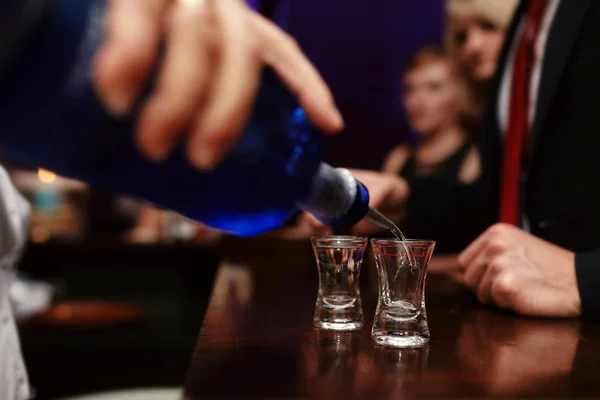 Erős alkoholtartalmú italt öntő csapos kis poharakba a bárban, italokba egy nightclubban vagy bárban — Stock Fotó