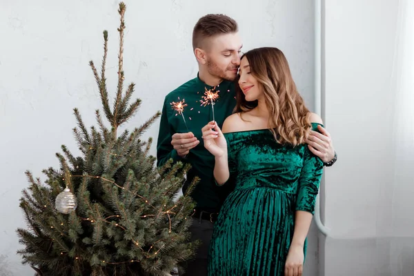 Brucia scintille nelle mani degli ospiti della festa. Coppia di persone stanno celebrando il Natale e le vacanze felicemente vicino all'albero di Natale splendidamente decorato, concetto di Natale — Foto Stock