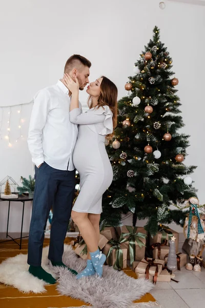 Photo de famille de Noël avec arbre de Noël et ornements, sol en bois et cheminée. L'homme et la femme s'embrassent près de l'arbre de Noël . — Photo