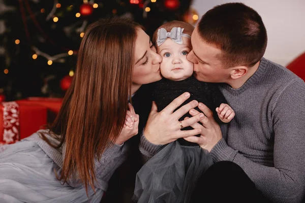 O pai e a mãe a beijarem a filha. Belos pais jovens estão beijando sua filhinha fofa, que está olhando para a câmera e sorrindo — Fotografia de Stock