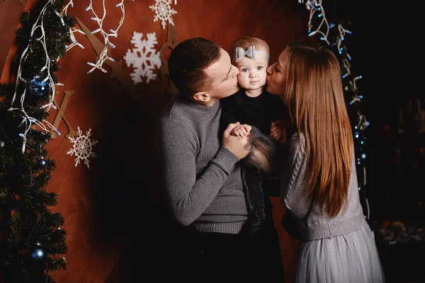 O pai e a mãe a beijarem a filha. Belos pais jovens estão beijando sua filhinha fofa, que está olhando para a câmera e sorrindo — Fotografia de Stock