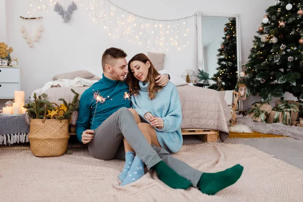 Fénykép a stílusos szerető férfi és terhes nő csillagszórókkal a háttérben a karácsonyi dekorációk — Stock Fotó