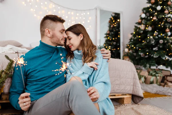 Noel süslemelerinin arka planında maytap olan şık bir adam ve hamile bir kadının fotoğrafı. — Stok fotoğraf