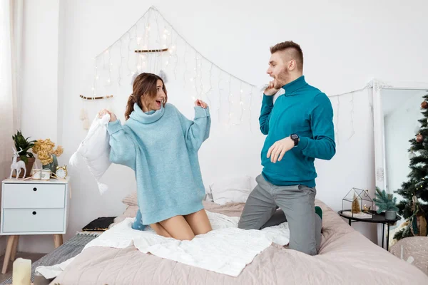 Szczęśliwa stylowa kochająca się para walcząca na poduszki w łóżku. Młody mężczyzna i kobieta spodziewają się dziecka na Święta. Skupienie selektywne — Zdjęcie stockowe