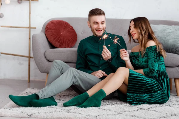 Glückliches Paar in stilvoller grüner Kleidung mit Wunderkerzen. Mann und schwangere Frau sitzen neben Sofa. Valentinstag — Stockfoto