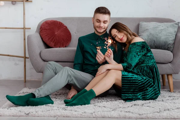 Casal feliz em roupas verdes elegantes com sparklers. Homem e mulher grávida sentados perto do sofá. Dia dos Namorados — Fotografia de Stock