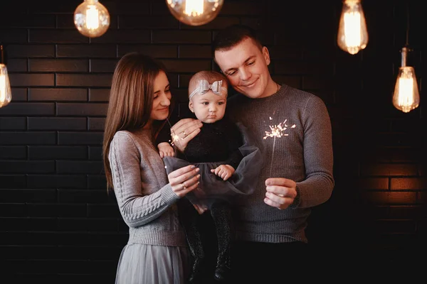 Retrato de família feliz, mãe, pai e bebê menina com faíscas na frente. família em antecipação do Natal. foto seletiva . — Fotografia de Stock