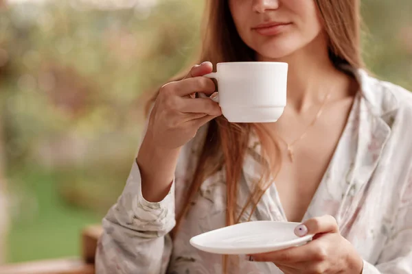 Porträt einer jungen Frau auf dem Balkon, die morgens eine Tasse Kaffee oder Tee hält. sie im Hotelzimmer mit Blick auf die Natur im Sommer. Mädchen trägt stylische Nachtwäsche. Entspannungszeit — Stockfoto