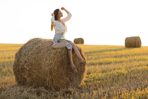 Porträt eines schönen Mädchens auf Heuhaufen auf einem abgeernteten Weizenfeld im Sommer. Selektiver Fokus. — Stockfoto